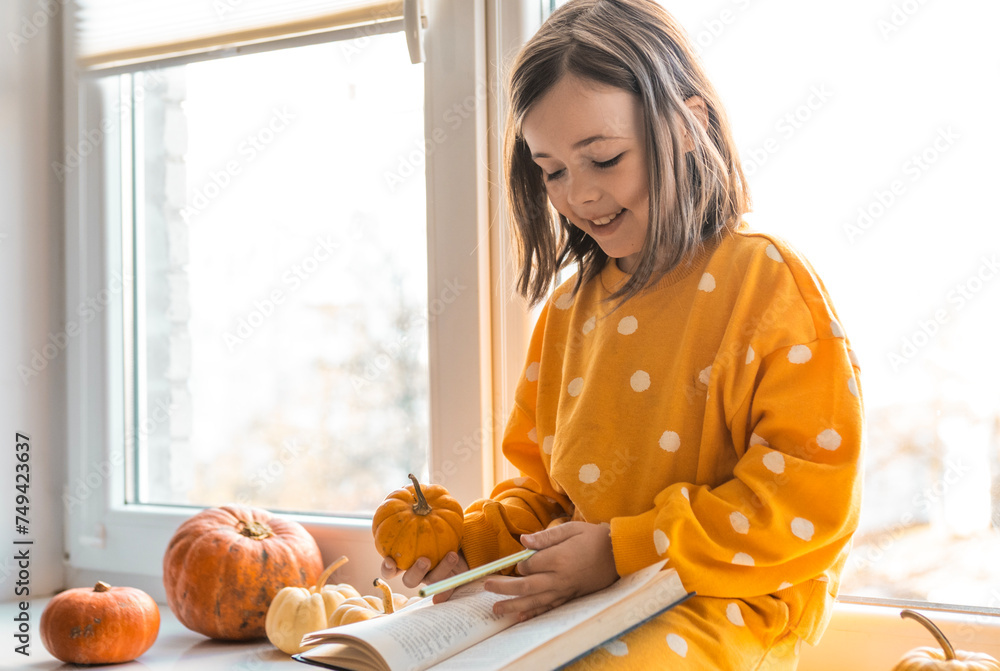 Cute little girl in an orange costume sits with decorative pumpkins on ...