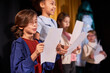 © Seventyfour - Side view portrait of young boy rehearsing lines standing on stage in school theater in row with children actors