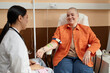 © Seventyfour - Portrait of smiling bald woman receiving chemotherapy treatment in procedure room at clinic and talking to nurse