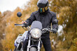 motorcyclist in a motorcycle jacket and tinted helmet with a classic motorcycle in nature. Stylish biker