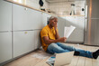 © Marko Geber - Stressed man sitting on kitchen floor with bills and laptop
