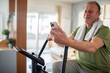 © Marko Geber - Middle aged man using smartphone on home exercise bike