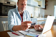 © Marko Geber - Middle aged man holding a credit card using laptop at home