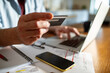 © Marko Geber - Cropped man holding a credit card using laptop at home