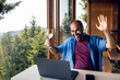 © Davor - Man having a virtual toast during video call in a home with forest in the background