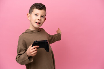 Wall Mural - Little caucasian boy playing with a video game controller isolated on pink background extending hands to the side for inviting to come