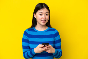 Wall Mural - Young Chinese woman isolated on yellow background sending a message with the mobile