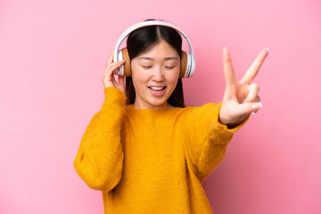 Poster - Young Chinese woman isolated on pink background listening music and singing