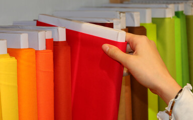 young girl choosing red color fabric in the haberdashery with many colorful fabrics