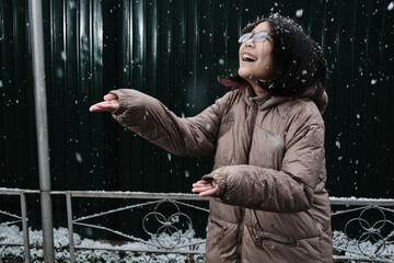 The happy girl in glasses holds out her palms to the falling snowflakes