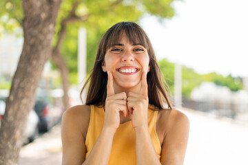 Young woman at outdoors smiling with a happy and pleasant expression