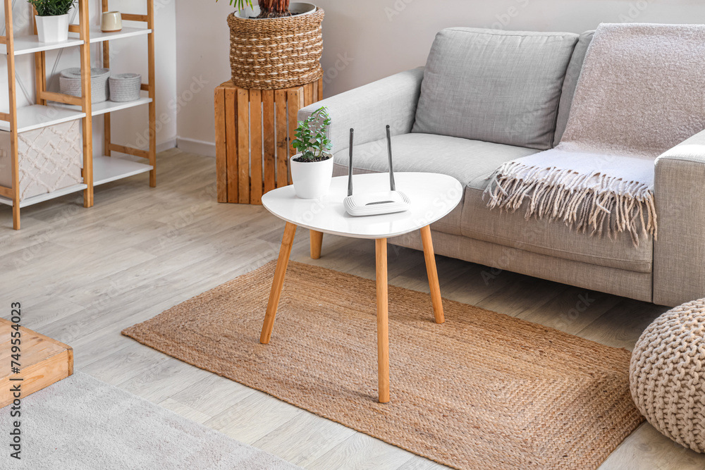 Modern wi-fi router with plant on table in living room interior