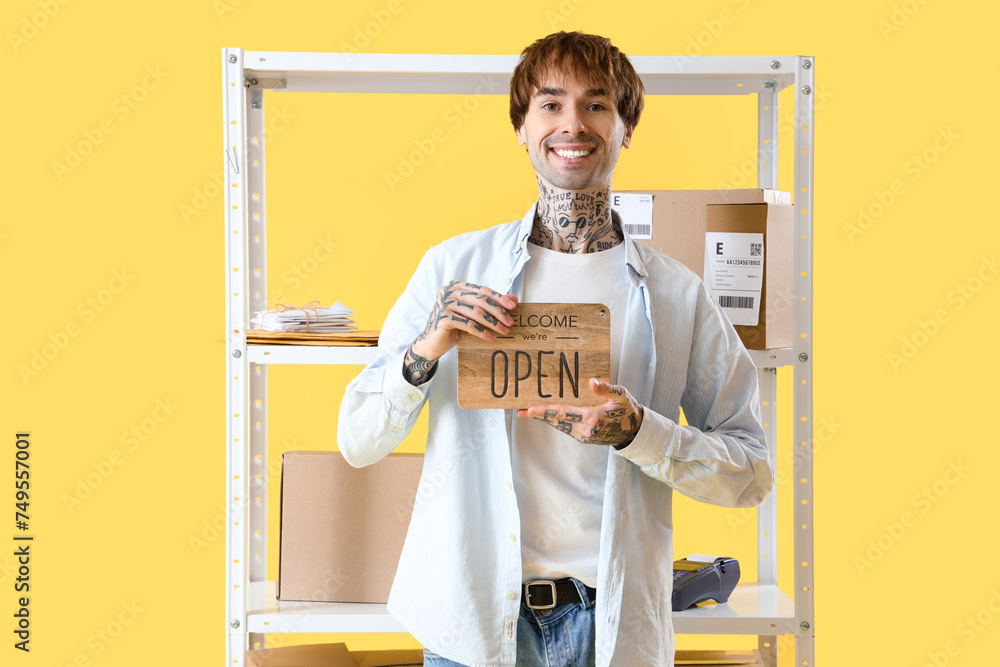 Young online store seller with OPEN sign and parcel boxes on yellow background