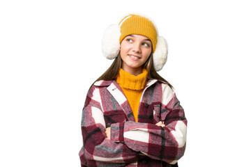 Poster - Teenager caucasian girl wearing winter muffs over isolated background looking up while smiling