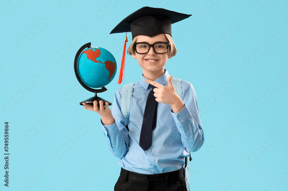 Little boy in graduation hat pointing at globe on blue background. End of school year