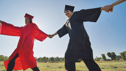 Wall Mural - College graduates holding hands run in a round dance.