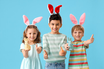 Wall Mural - Cute little children in bunny ears with toys rabbit showing thumb-up gesture on blue background. Easter celebration