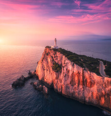 Wall Mural - Aerial view of lighthouse on the mountain at colorful sunset in summer. Beautiful lighthouse on the rock, cliffs, sea, sky with pink and purple clouds at dusk. Top view of Cape Lefkada, Greece. Beacon