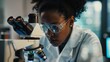 An African American woman scientist examining samples through a microscope in a laboratory.
