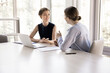 © fizkes - Two young pretty female colleagues talking met in modern boardroom, client and company representative negotiating in office, share information, provide assistance, sell services, engaged in teamwork