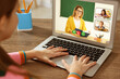 © New Africa - E-learning. Little girl using laptop during online lesson at wooden table indoors, closeup