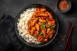 Sweet and sour chili sauce chicken with rice in a plate on a black stone table, top view