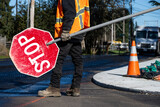 Fototapeta Desenie - Traffic control worker in orange reflective safety vest with temporary stop sign managing traffic in a road work construction zone
