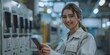 © Attasit - Factory woman worker standing in front Employee Attendance System, using a smartphone, looking at a smartphone, smiling happy