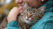 Woman cuddling a content tabby cat, close-up on pet's face with eyes closed.