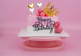 Birthday cake with gold crown and hearts on pink background.	