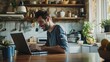 © KKC Studio - A man focused on his laptop in the kitchen.