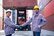 Engineers shaking hands congratulating themselves on success with shipping containers in the background.