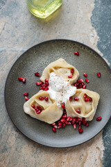 Wall Mural - Manti served with pomegranate seeds and yogurt, vertical shot on a beige and grey granite background, elevated view