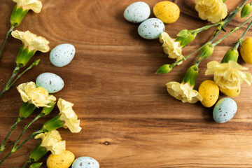 Wall Mural - Yellow flowers and pastel yellow and blue colored eggs on a background of brown wood. Layout. Mockups. Springs background. Easter background. Easter eggs close up