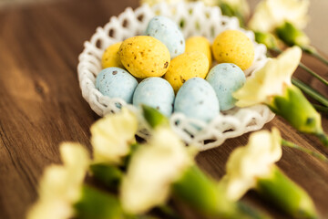 Wall Mural - Yellow flowers and pastel yellow and blue colored eggs in a white small wicker basket on a background of brown wood. Layout. Mockups. Pastel Springs background. Easter background. Easter eggs close up