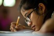 © Yuliia - Close up side view tired young little girl Indian Arabian ethnic kid child studying hard lying on desk writing pencil homework upset bored schoolgirl education troubles indoors school classroom lesson
