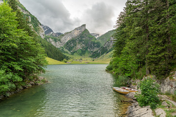 Wall Mural - Beautiful summer view on lake Seealpsee in the Swiss alps, 2 rowing boats are lying in the water in the foreground. Cloudy sky. Wonderful hiking spot. Alpine lake with high mountains. Pine trees.