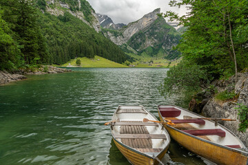 Wall Mural - Beautiful summer view on lake Seealpsee in the Swiss alps, 2 rowing boats are lying in the water in the foreground. Cloudy sky. Wonderful hiking spot. Alpine lake with high mountains. Pine trees.