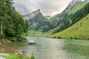 Wall Mural - Beautiful summer view on lake Seealpsee in the Swiss alps.. Cloudy sky. Wonderful hiking spot. Alpine lake with high mountains. Pine trees. Appezell mountains in Switzerland.