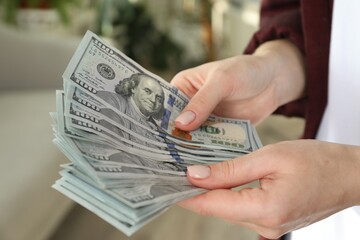 Money exchange. Woman counting dollar banknotes on blurred background, closeup