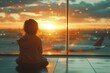 Back view of a young child sitting at an airport terminal, gazing at airplanes against a beautiful sunset backdrop.
