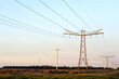 High voltage pole with power transmission  lines crossing  wind turbine  field in the background.