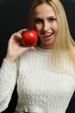 Fototapeta Mapy - Beautiful young woman holds an apple near her face, smiles, looks at the camera.