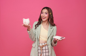 Young asian teen woman holding piggy bank and calculator isolated on pink background. calculation tax concept.