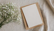 Mock up of blank paper card, craft envelope and gypsophila flowers on neutral beige linen texture