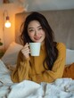 Junge Frau mit asiatischen Wurzeln sitzt in ihrer Wohnung auf dem Bett mit einer großen Tasse Kaffee