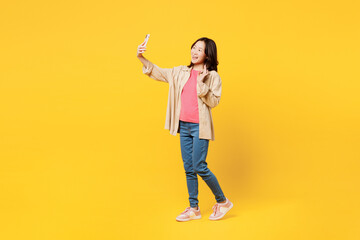 Wall Mural - Full body young woman of Asian ethnicity wear pink t-shirt beige shirt casual clothes do selfie shot on mobile cell phone post photo on social network waving hand isolated on plain yellow background.