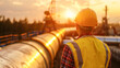 A man in a yellow safety vest stands in front of a large pipe. The sun is setting in the background, casting a warm glow over the scene. The man is a worker