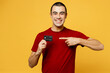 Young smiling happy middle eastern man he wears red t-shirt casual clothes hold in hand point finger on mock up of credit bank card isolated on plain yellow orange background studio Lifestyle concept