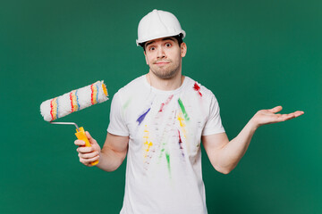 Canvas Print - Young employee laborer handyman man wear stained t-shirt hardhat hat hold paint roller spread hands isolated on plain green background. Instruments for renovation apartment room. Repair home concept.